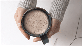 Overhead view of woman holding mug of hot chocolate over  gray autumn background