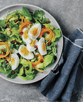 A bowl of fresh salad with boiled eggs  carrots  and pomegranate seeds on gray background