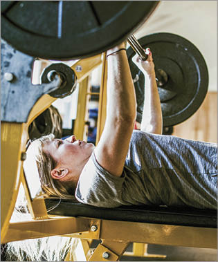 A young woman exerts strength and power on a bench press at the gym   Horizontal image with copy space 