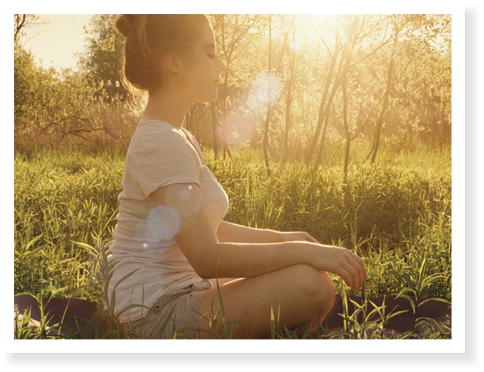 Young woman sitting on yoga mat i field by sunset 