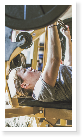 A young woman exerts strength and power on a bench press at the gym   Horizontal image with copy space 