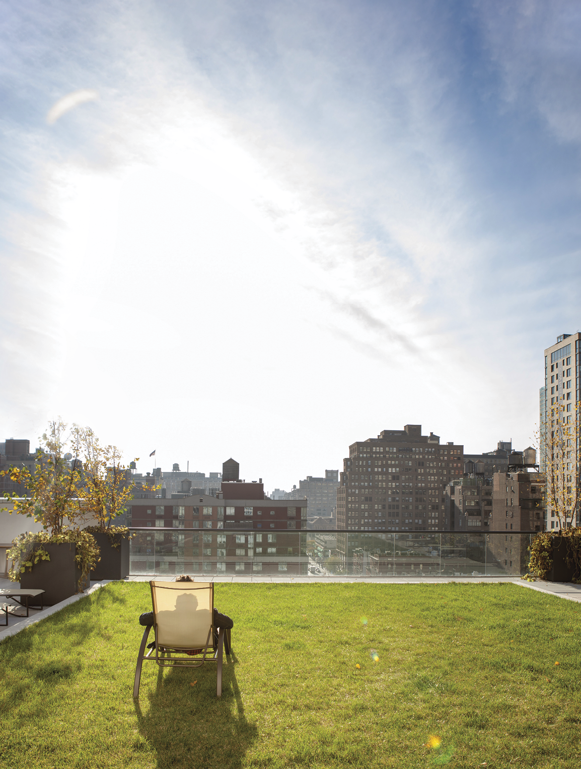 Person sitting in lounge chair on the grass viewing cityscape from rooftop