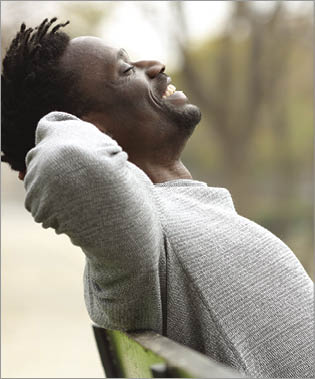Side view portrait of a happy black man relaxing sitting on a bench in a park
