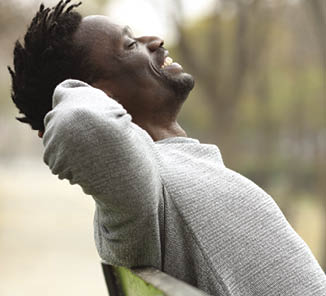 Side view portrait of a happy black man relaxing sitting on a bench in a park