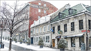 Montreal, Canada - February 6, 2016: Historic architecture in travel destination, Old Montreal is surrounded with falling snow on a cold winter day. Businesses including restaurants and retail shops remain open. The streets are empty.  In the background a few people walk the snow covered sidewalks. 