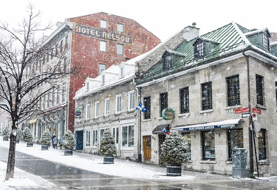 Montreal, Canada - February 6, 2016: Historic architecture in travel destination, Old Montreal is surrounded with falling snow on a cold winter day. Businesses including restaurants and retail shops remain open. The streets are empty.  In the background a few people walk the snow covered sidewalks. 