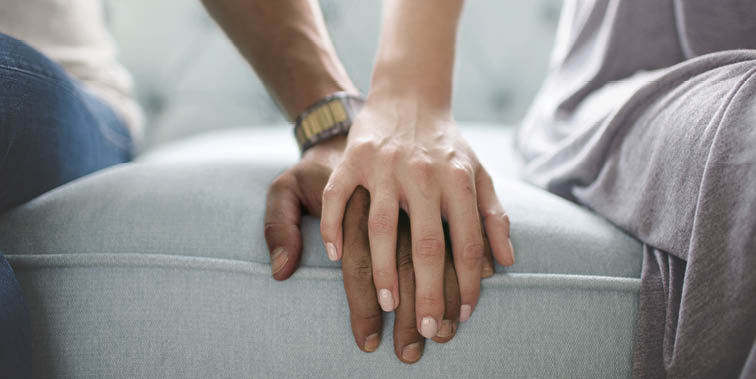 Waist photo of man and woman holding hands while sitting on a couch