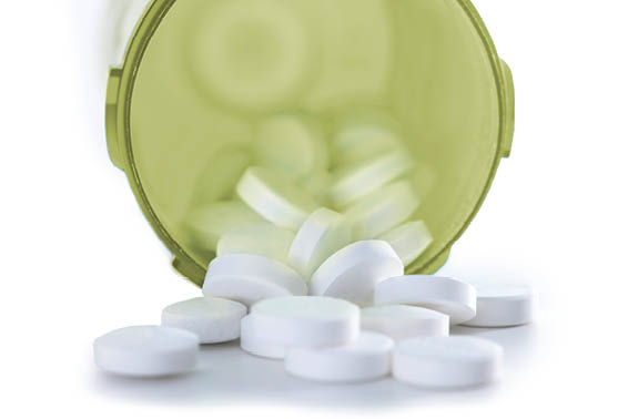 Pills spilling from a green bottle on white background