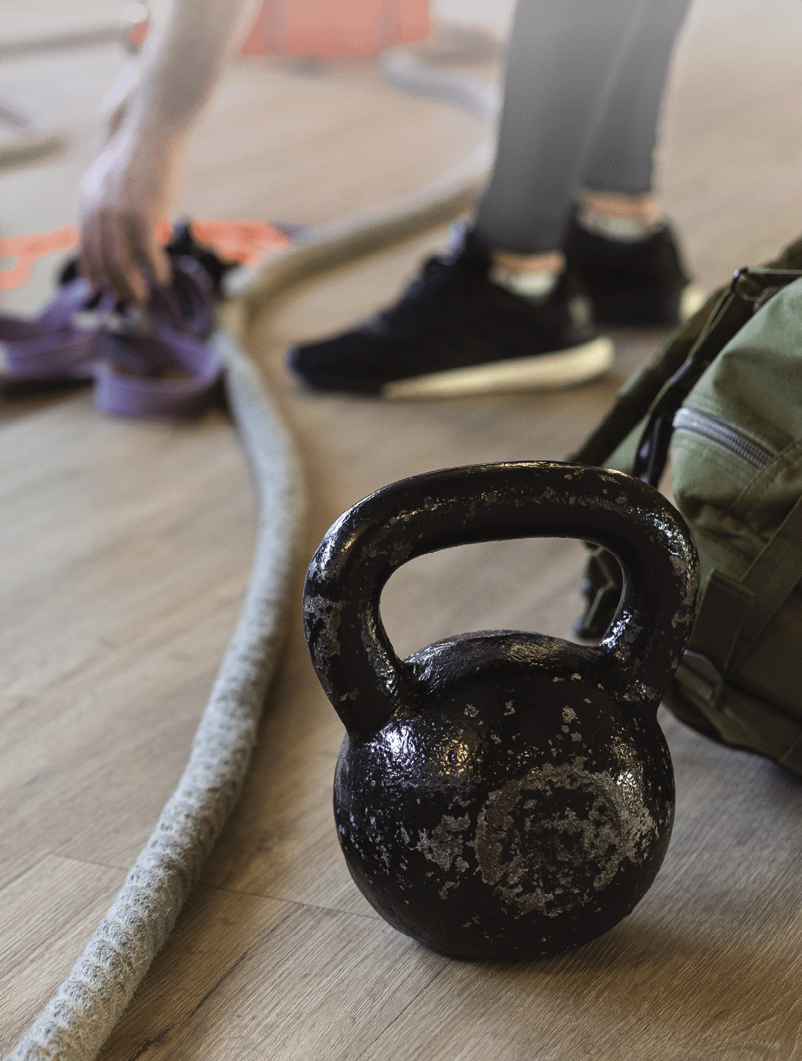 Preparing gym equipment for boot camp and work out with kettle bell, rope, sandbag in gym hall on the floor  Instructor's legs in background 