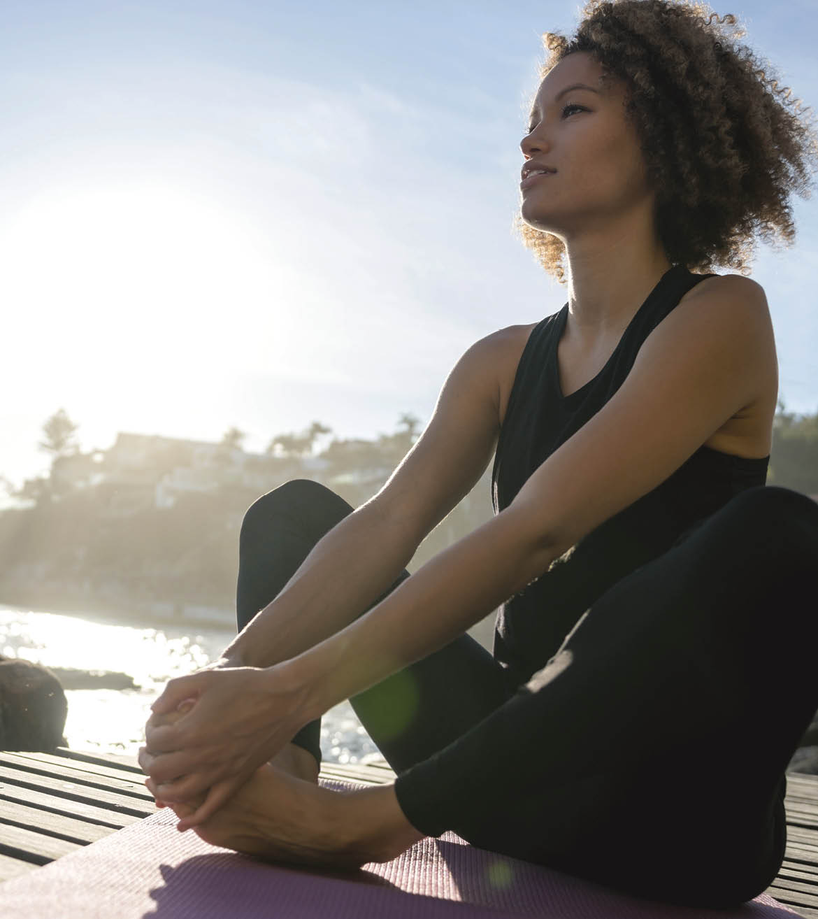 Woman doing yoga exercises by the beach and sitting on a yoga mat