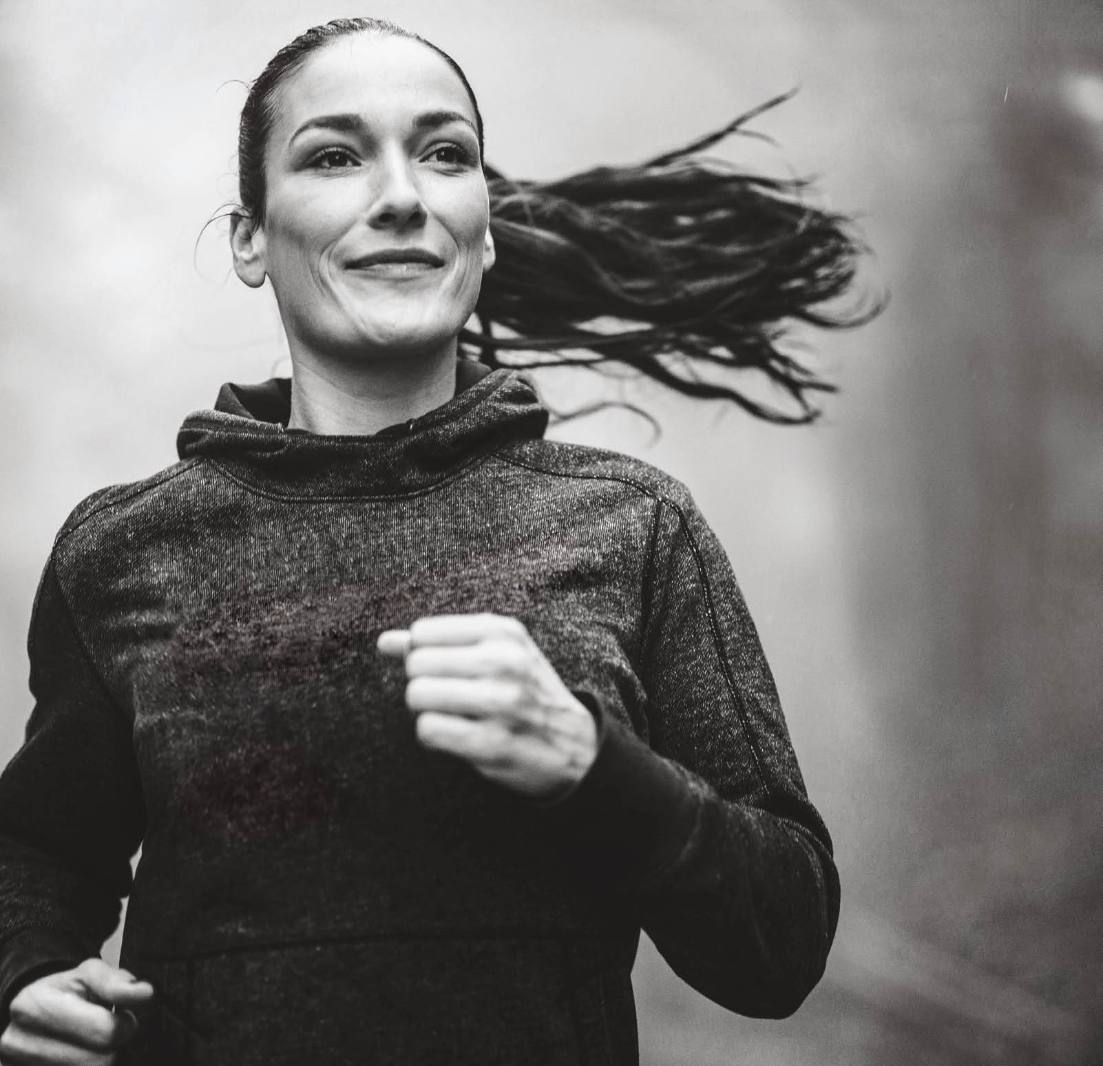 Young smiling female athlete jogging on a rainy day during autumn in foggy nature 