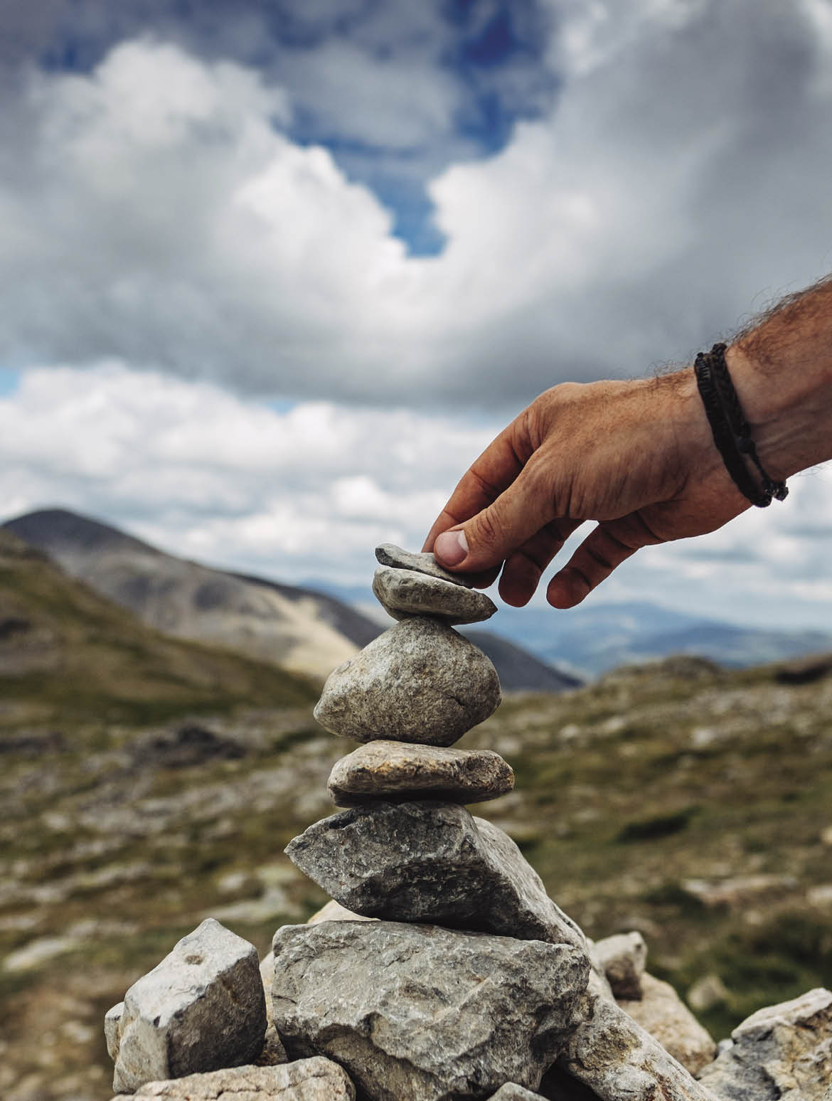 A hand placing a small stone on top of a cairn stone pile during a hike on Scafell pike mountain in the lake district