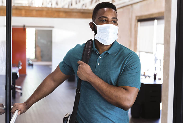 A mid adult businessman leaves his office wearing a protective face mask at the end of the work day 