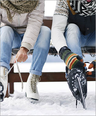Unrecognizable couple sitting on bench and tying ice skates outdoors in winter