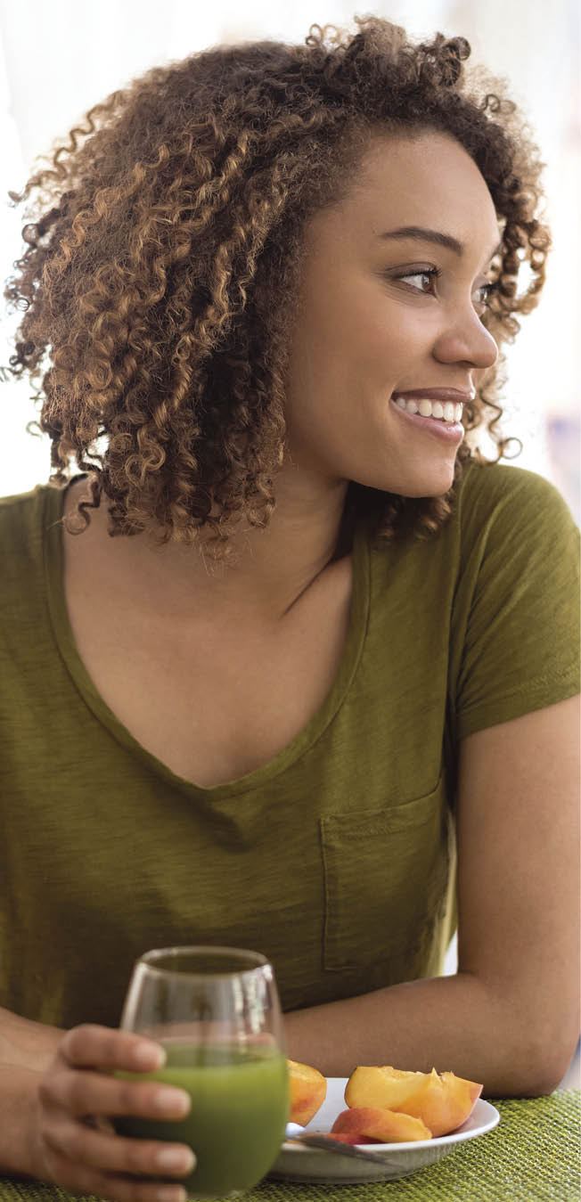 Happy woman at home having a green juice for breakfast with some fruit