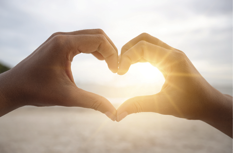 The hands of women and men are the heart shape with the sun light passing through the hands