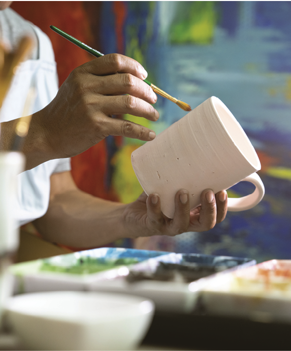 Closeup shot of a man painting a cup in her small crafts workshop