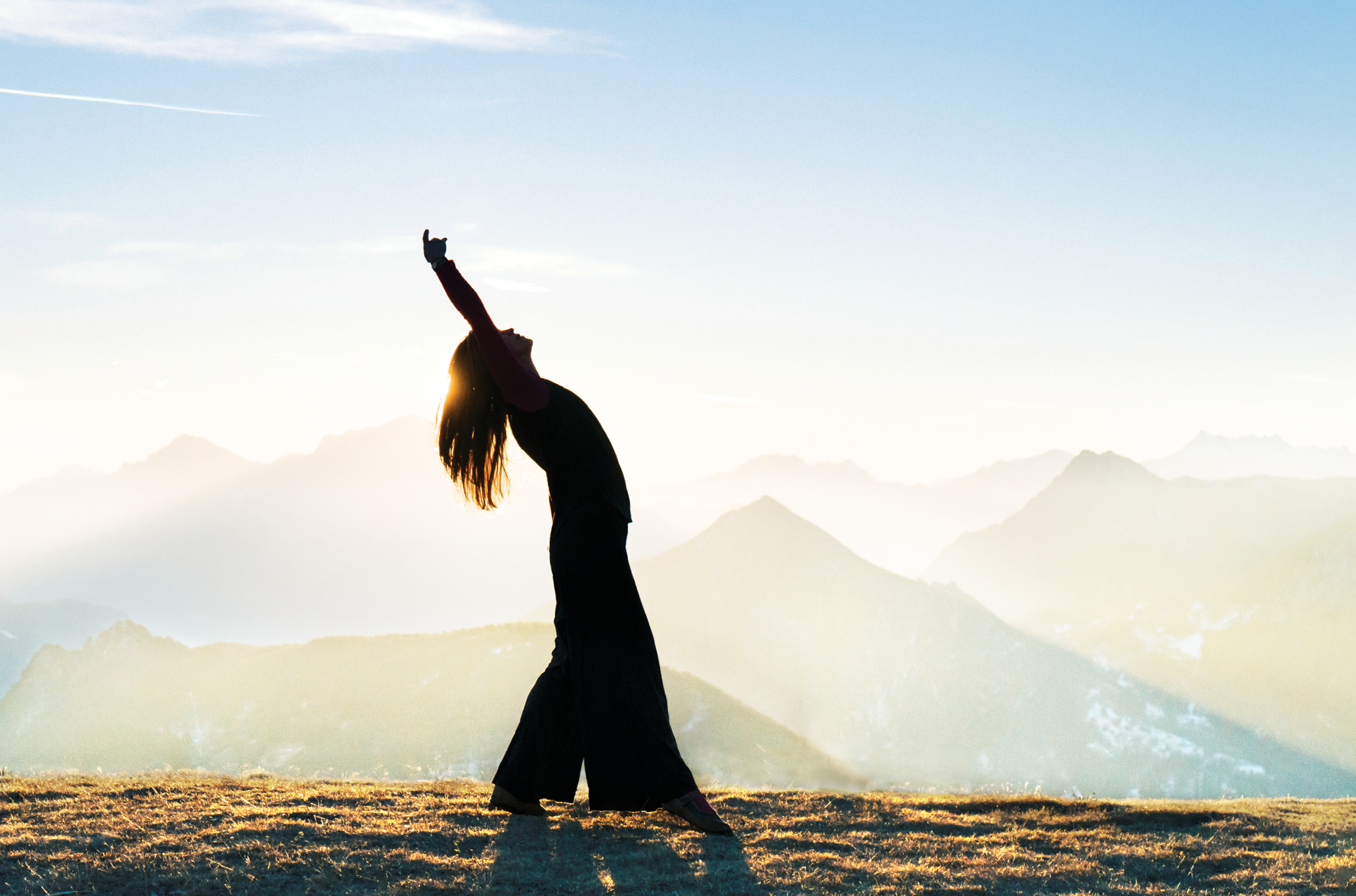 She is bending backwards as sun rises behind her   She is in an open meadow, Ticino Canton