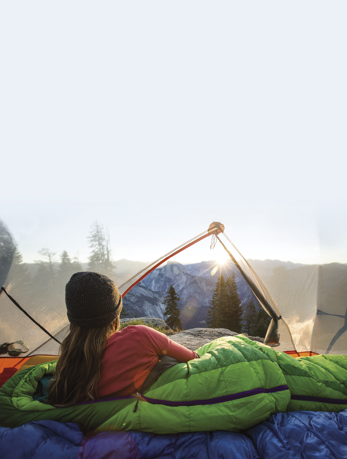 A woman taking in the view of Half Dome from insider her tent while camping in the mountains 