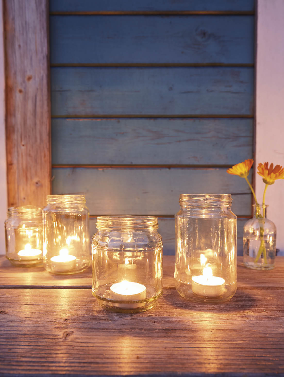 Still life of candles in jars on wooden table in the evening in summer