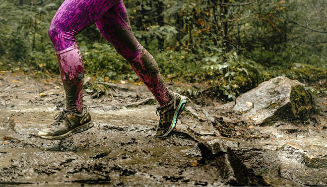 woman runs over rocks in forest legs in spray dirt