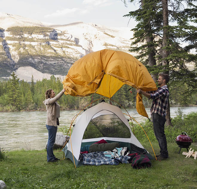 Couple assembling tent at campsite near mountains