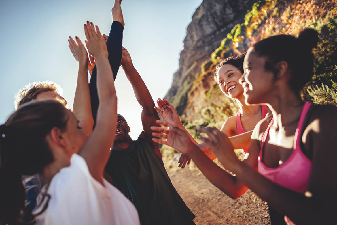 Multi-ethnical group of young adult runners cheering and high fiving after a good run outdoors