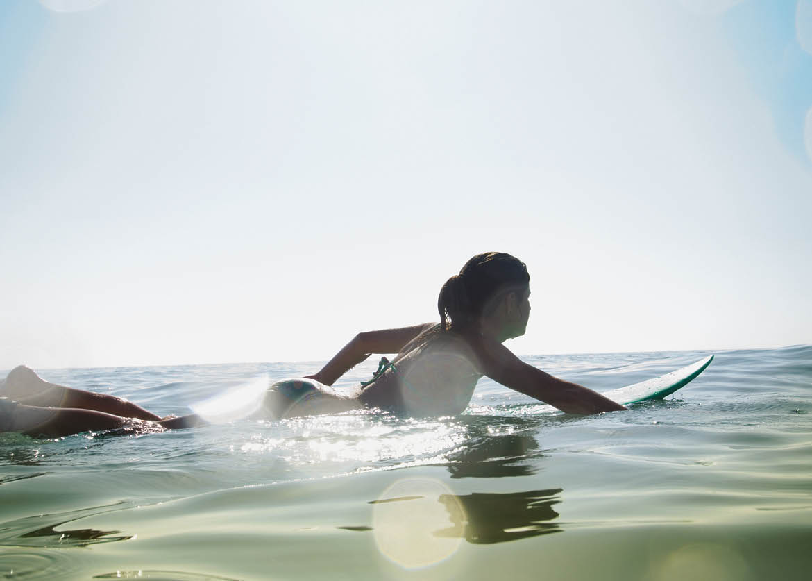 Hispanic girl paddling on surfboard