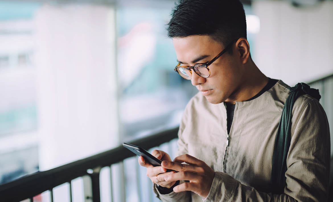 Smart young man text messaging on mobile phone on the way to work on urban bridge in city in the morning