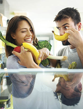 Closeup of a cheerful young couple picking some fruit and veggies from the fridge to make some healthy breakfast on Sunday morning  Shot from inside the working fridge 