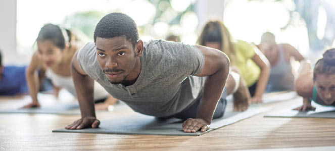 A multi-ethnic group of adults are taking a yoga class together  They are holding plank position on their yoga mats 