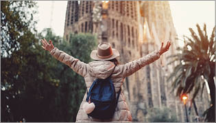 Rear view of young woman in front of Sagrada Familia with arms outstretched enjoying the beautiful city