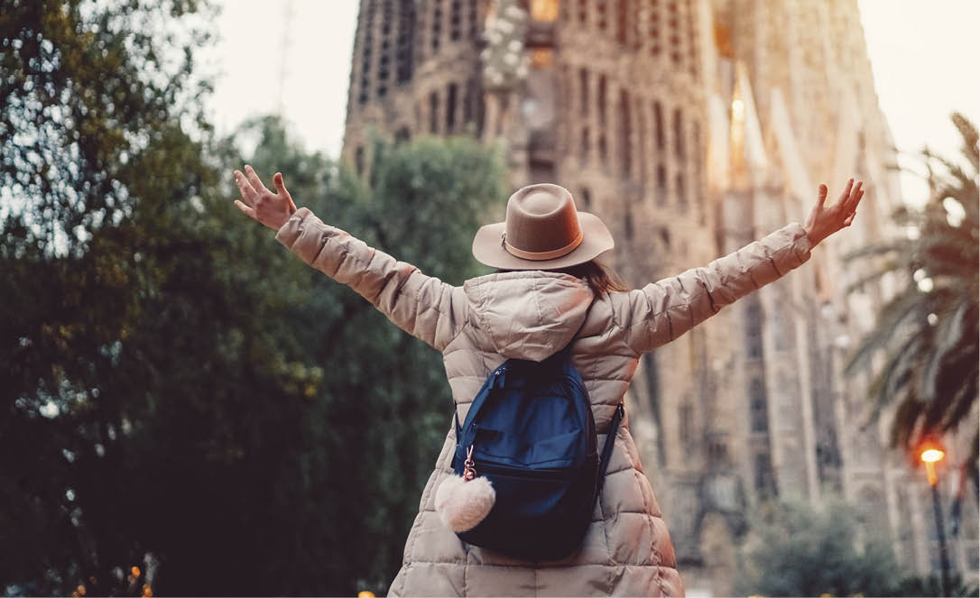 Rear view of young woman in front of Sagrada Familia with arms outstretched enjoying the beautiful city