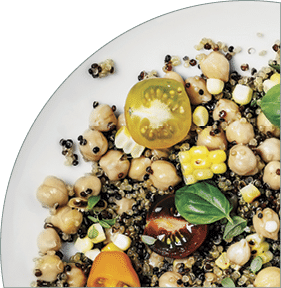 A bowl of quinoa salad  two spoons  and a salt shaker on white background