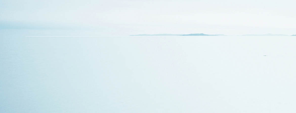Woman standing on stone pathway in lake with arms outstretched and scarf blowing in wind