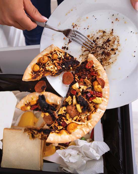 Close-up Of A Person Throwing Pepperoni Pizza On Plate In Dustbin