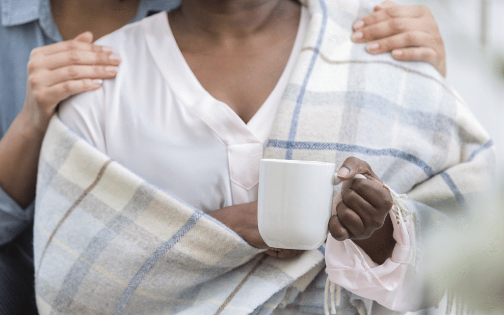 Unrecognizable woman comforts her friend who is ill  She gives her a warm blanket and a cup of hot tea 