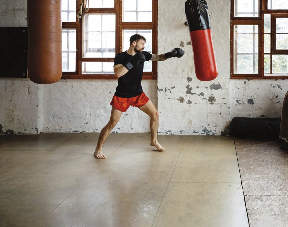 Male muay thai boxer training on sandbag in a gym