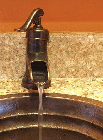 Vertical image of water running out of a faucet into a copper sink   Marble surround and orange wall 