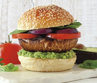 Portobello mushroom vegan burger with avocado, tomato, spinach and onion on a marble serving board against a white wood background