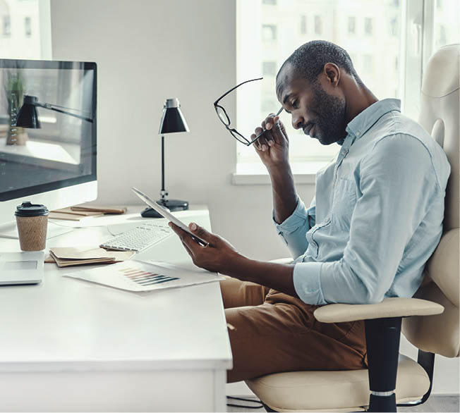 Concentrated young African man in shirt using digital tablet while working in the office