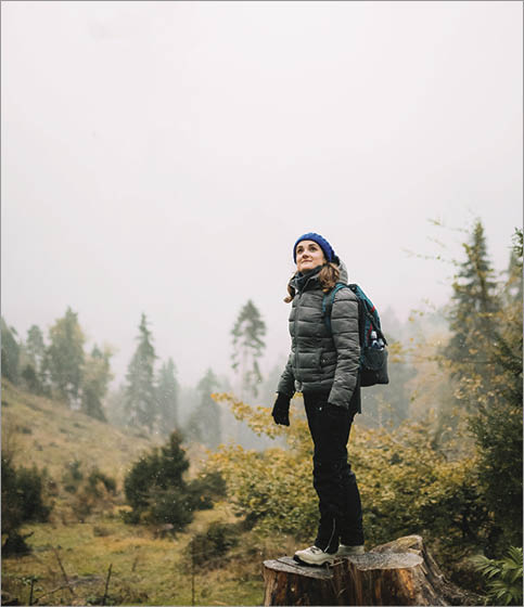 Young Woman Standing On Stump In Forest And Looking Up 