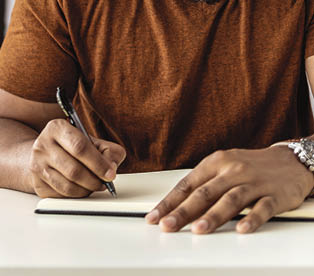 Image of happy African man with notepad and pen sitting on sofa 