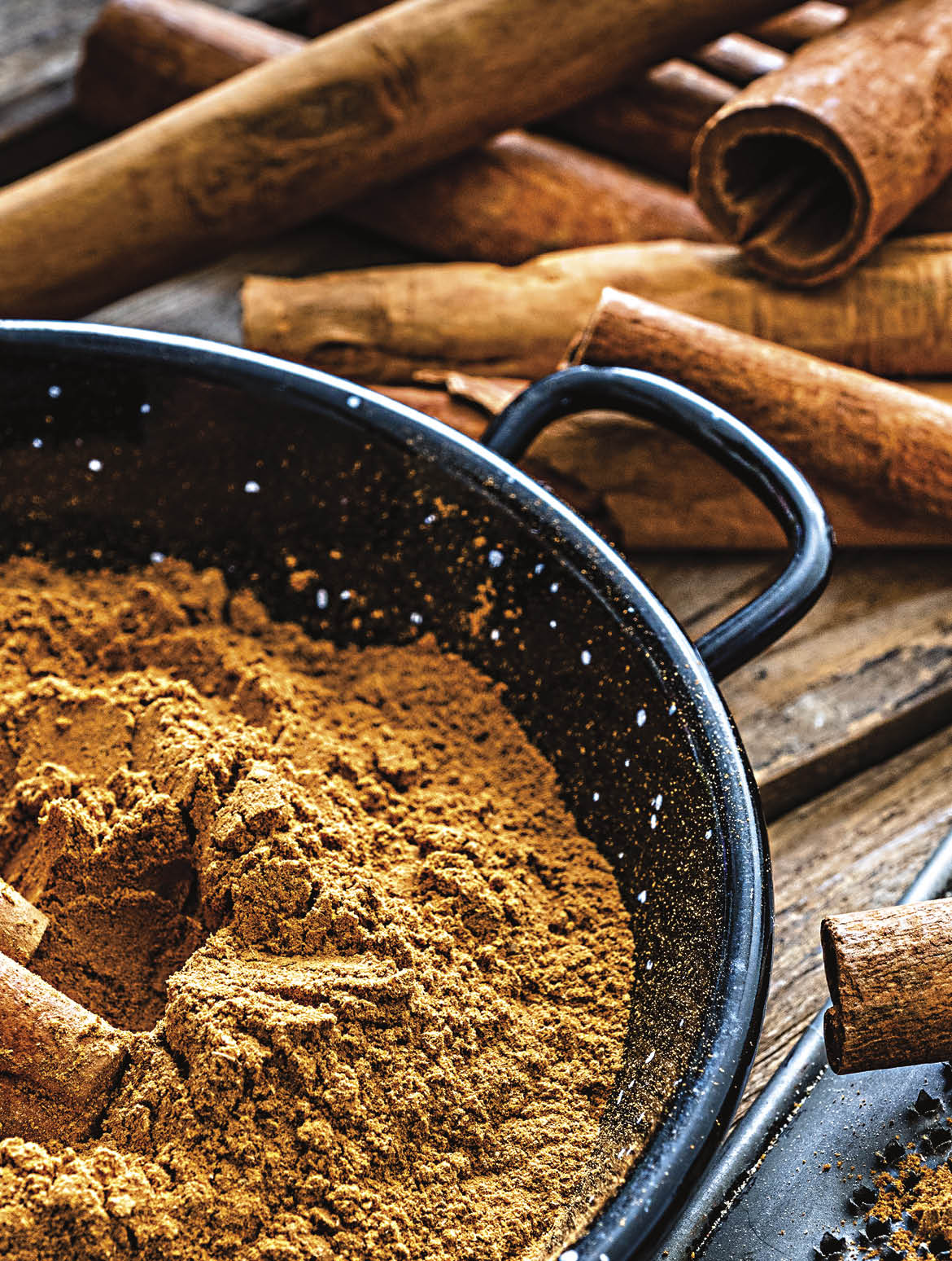 High angle view of a rustic wooden table with cinnamon sticks and ground cinnamon  A small grater is in a container filled with ground cinnamon  Predominant color is brown  High resolution 42Mp studio digital capture taken with SONY A7rII and Zeiss Batis 40mm F2 0 CF lens
