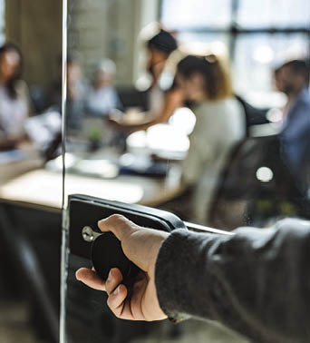 Close up of unrecognizable male person opening glass door to enter the office  There are people in the background 