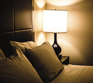 Illuminated lamp and bed in dimly lit bedroom at night